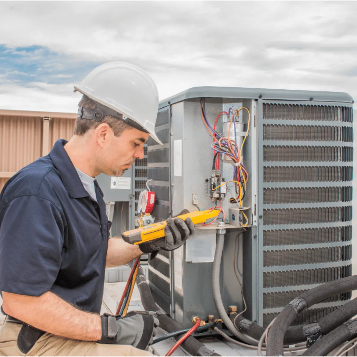 HVAC technician in a hard hat testing an outdoor air conditioner with a multimeter